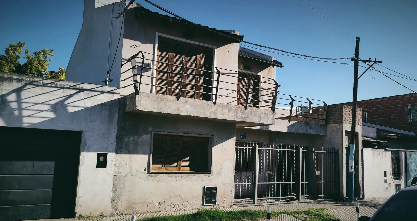 A two-storey house with shutters and an iron balcony under a hard blue sky, in Rosario.