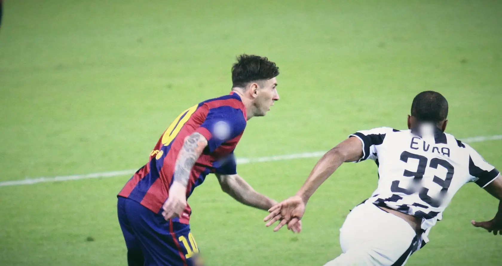 Messi in Barcelona colours chasing alongside a Juventus player on open green.