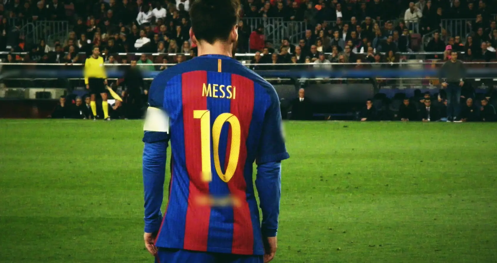 Messi seen from behind in a Barcelona shirt with a yellow 10, stands and a linesman ahead.