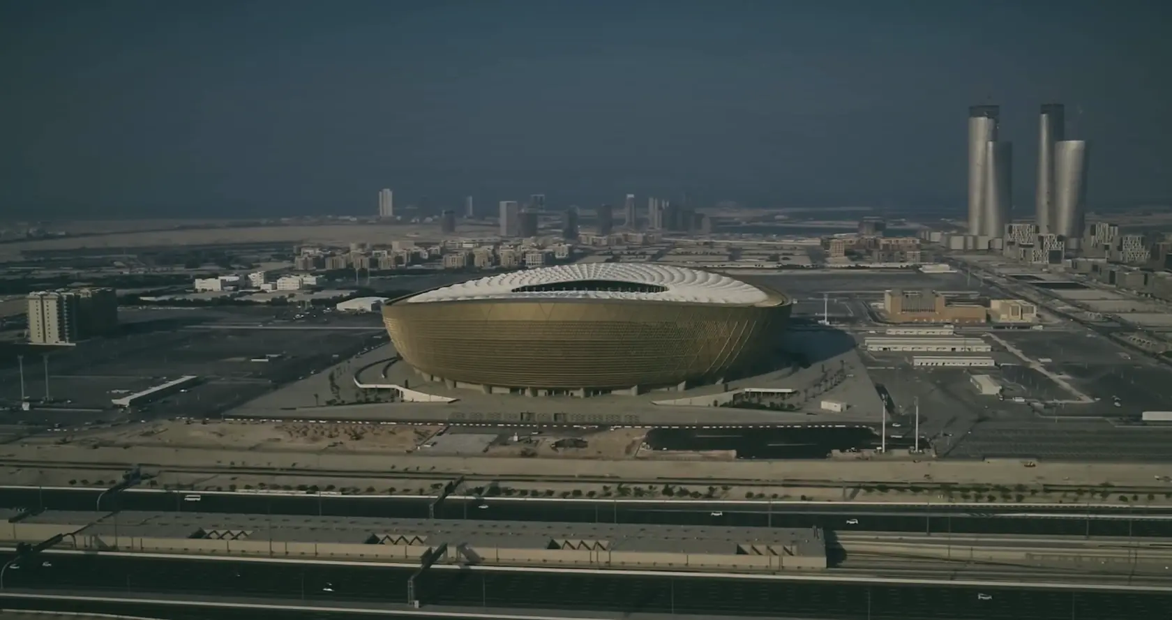 Aerial view of Lusail Stadium, Qatar, in daylight haze: a gold bowl in flat land.