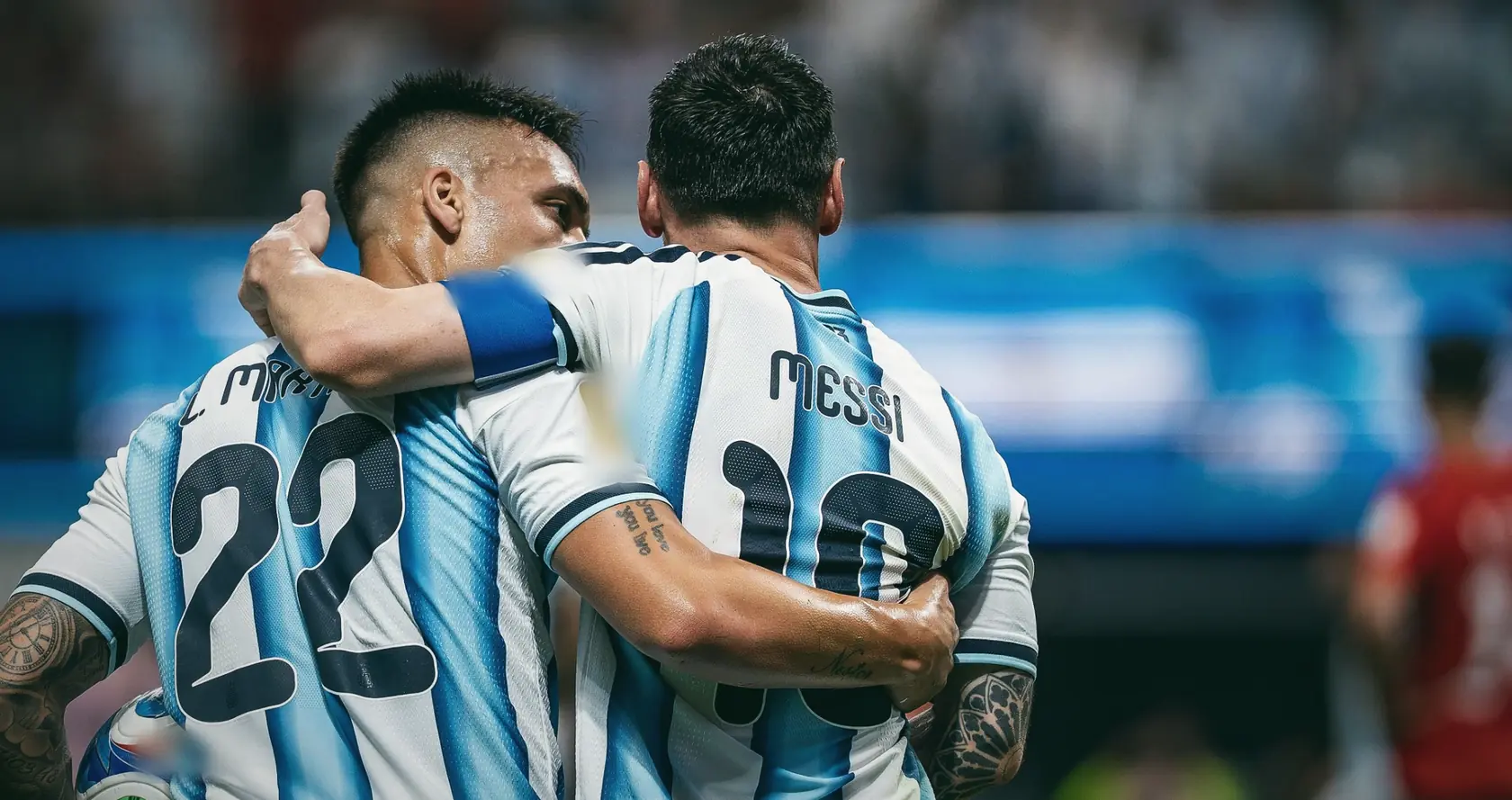 Lautaro Martinez with his arm around Messi, both seen from behind in Argentina stripes.