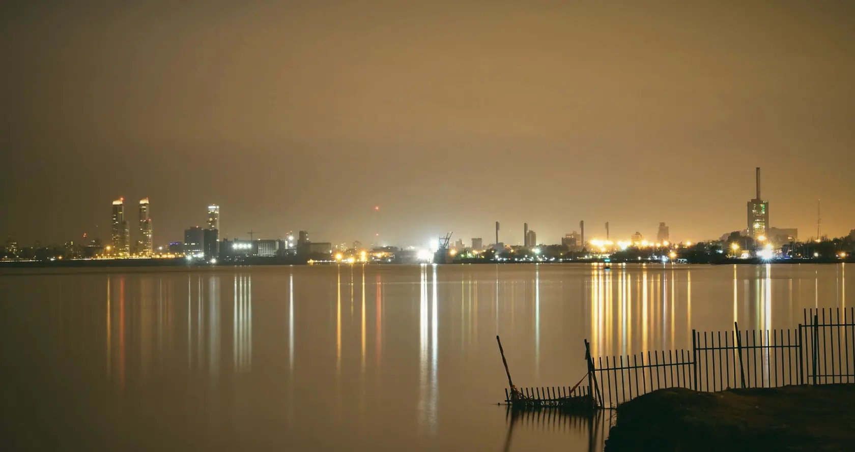 The Rosario riverfront at night, with lights across the water under an orange sky.