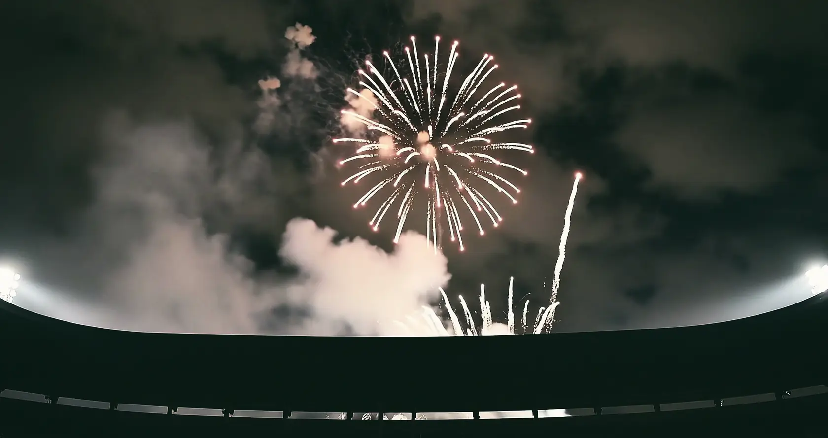 Fireworks and white smoke above the dark rim of a stadium.